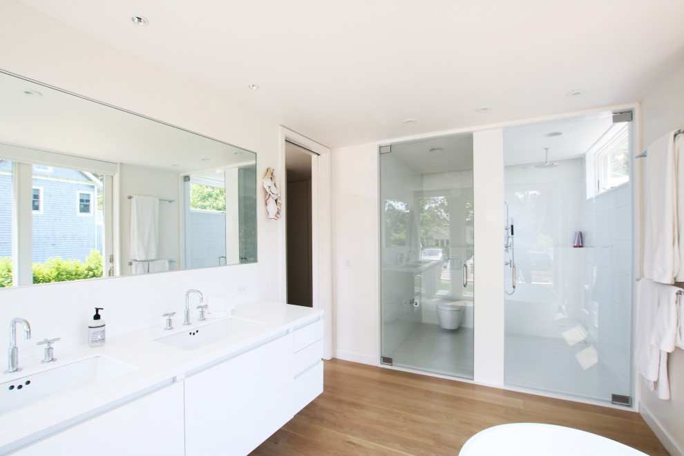 Bathroom - mid-sized modern master white tile and ceramic tile light wood floor and white floor bathroom idea in New York with flat-panel cabinets, white cabinets, a wall-mount toilet, white walls, an undermount sink, solid surface countertops, a hinged shower door and white countertops