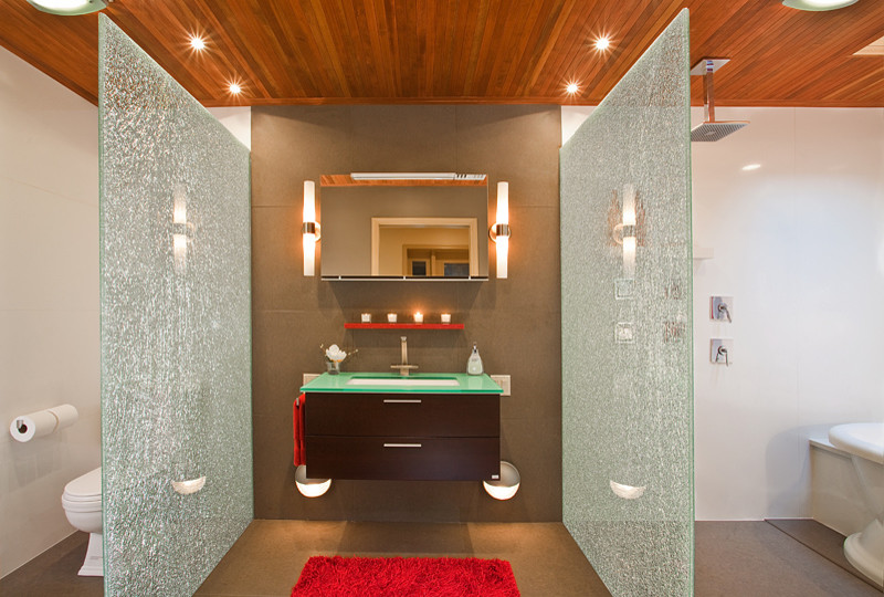 Idée de décoration pour une grande salle de bain principale minimaliste en bois foncé avec un lavabo suspendu, un placard à porte plane, un plan de toilette en verre, une baignoire en alcôve, une douche à l'italienne, WC à poser, un carrelage gris, des dalles de pierre et un mur gris.