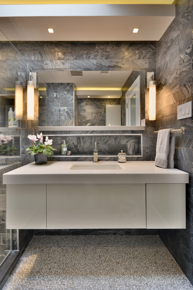 Photo of a medium sized modern ensuite bathroom in New York with flat-panel cabinets, white cabinets, an alcove shower, a one-piece toilet, grey walls, pebble tile flooring, a submerged sink, white floors, a hinged door, black tiles, marble tiles and engineered stone worktops.