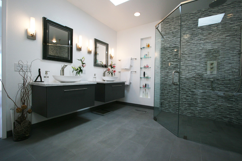 Exempel på ett stort modernt en-suite badrum, med ett fristående handfat, släta luckor, grå skåp, marmorbänkskiva, ett fristående badkar, en kantlös dusch, en vägghängd toalettstol, grå kakel, vita väggar och kalkstensgolv