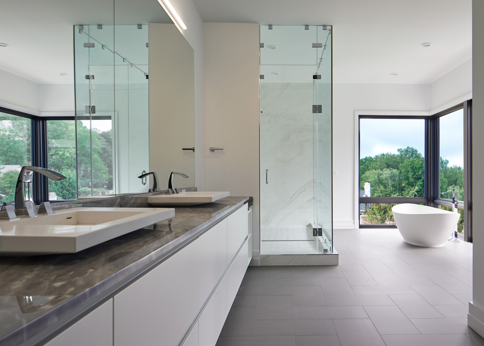 Modern inredning av ett mycket stort grå grått en-suite badrum, med släta luckor, vita skåp, ett fristående badkar, en dusch i en alkov, vit kakel, vita väggar, ett fristående handfat, grått golv och dusch med gångjärnsdörr