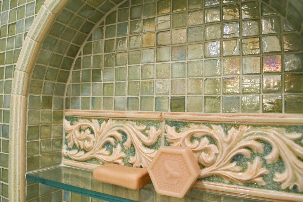 Пример оригинального дизайна: большая главная ванная комната в средиземноморском стиле с врезной раковиной, фасадами с утопленной филенкой, искусственно-состаренными фасадами, столешницей из искусственного камня, угловой ванной, душем над ванной, унитазом-моноблоком, зеленой плиткой, стеклянной плиткой, бежевыми стенами и полом из керамогранита