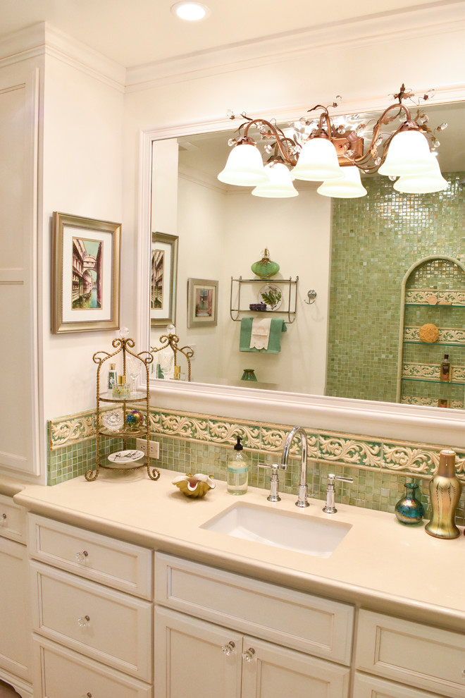 Example of a large tuscan master green tile and glass tile porcelain tile bathroom design in Los Angeles with an undermount sink, recessed-panel cabinets, distressed cabinets, solid surface countertops, a one-piece toilet and beige walls