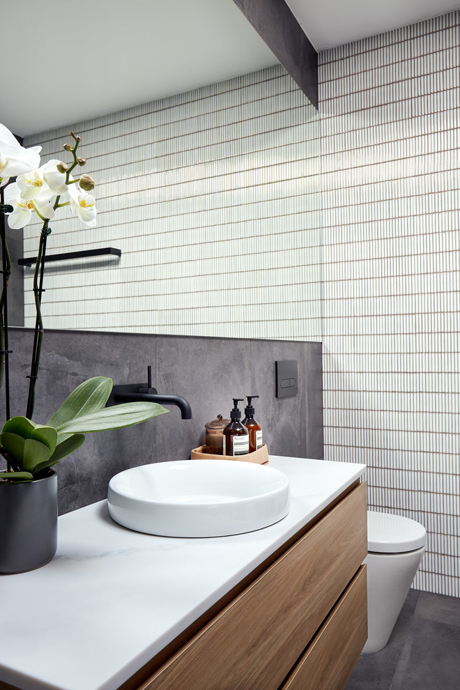 Modelo de cuarto de baño contemporáneo con armarios con paneles lisos, puertas de armario de madera oscura, baldosas y/o azulejos blancos, lavabo sobreencimera, suelo gris y encimeras blancas