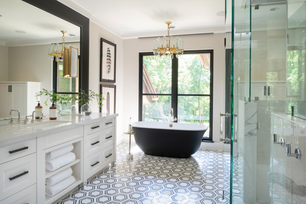 Klassisk inredning av ett vit vitt badrum, med luckor med infälld panel, vita skåp, ett fristående badkar, beige väggar, ett undermonterad handfat och flerfärgat golv