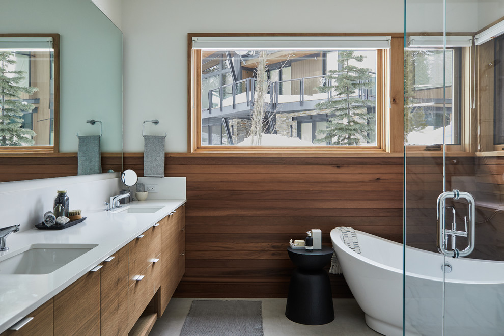 Aménagement d'une salle de bain contemporaine en bois brun avec un placard à porte plane, une baignoire indépendante, une douche d'angle, un mur gris, un lavabo encastré, un sol gris, une cabine de douche à porte battante et un plan de toilette blanc.