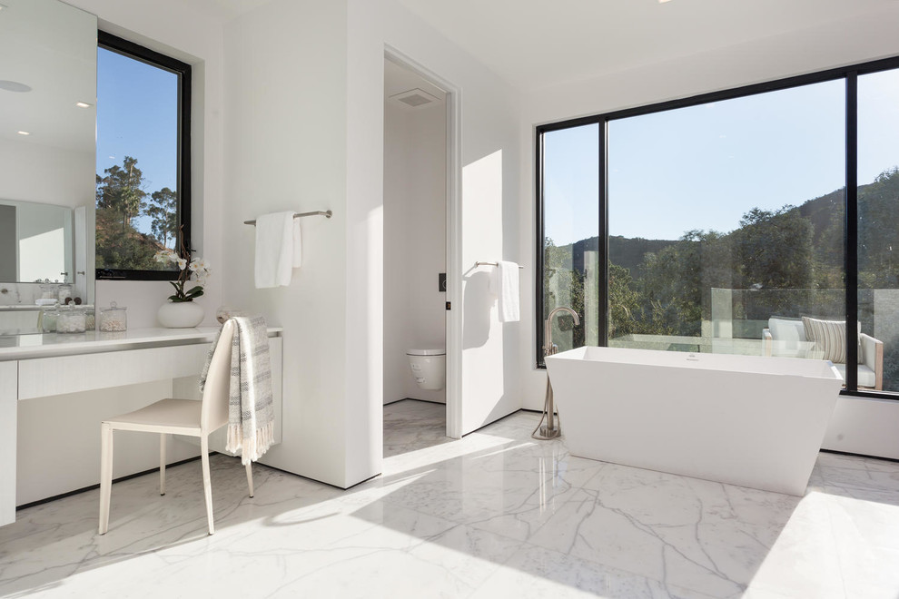 Inspiration for a large contemporary ensuite bathroom in Los Angeles with flat-panel cabinets, light wood cabinets, a freestanding bath, a wall mounted toilet, white walls, marble flooring, marble worktops and an enclosed toilet.