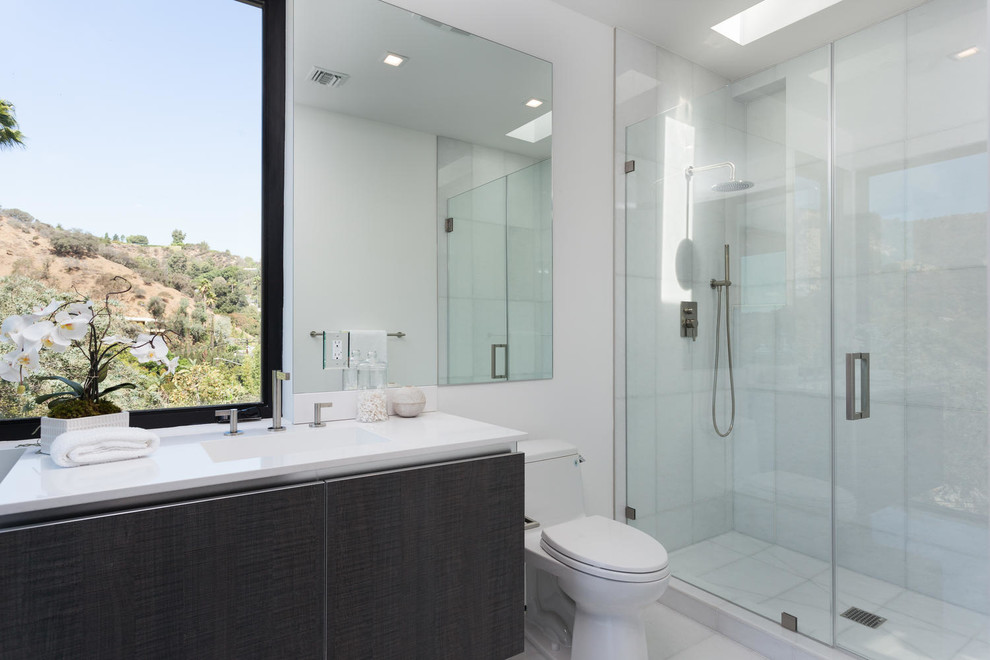Exempel på ett mellanstort modernt badrum med dusch, med släta luckor, skåp i mörkt trä, ett fristående badkar, en kantlös dusch, en vägghängd toalettstol, vit kakel, stenhäll, vita väggar, marmorgolv, ett undermonterad handfat och marmorbänkskiva