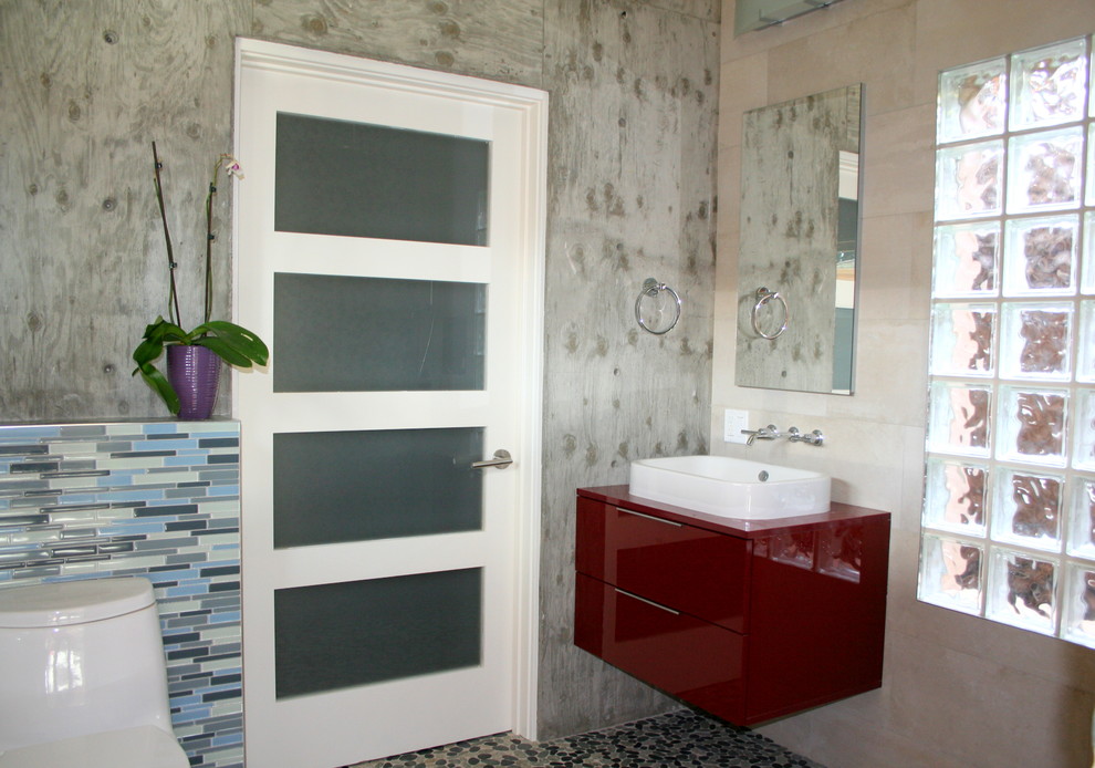 Aménagement d'une petite salle de bain moderne pour enfant avec une vasque, un placard à porte plane, des portes de placard rouges, une douche ouverte, WC séparés, un carrelage gris, une plaque de galets, un mur beige et un sol en galet.