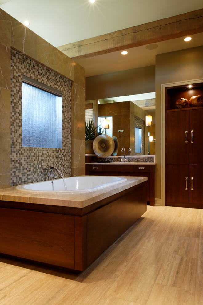 Expansive contemporary ensuite bathroom in Omaha with a submerged sink, flat-panel cabinets, dark wood cabinets, limestone worktops, a built-in bath, a double shower, beige tiles, stone tiles, beige walls and porcelain flooring.