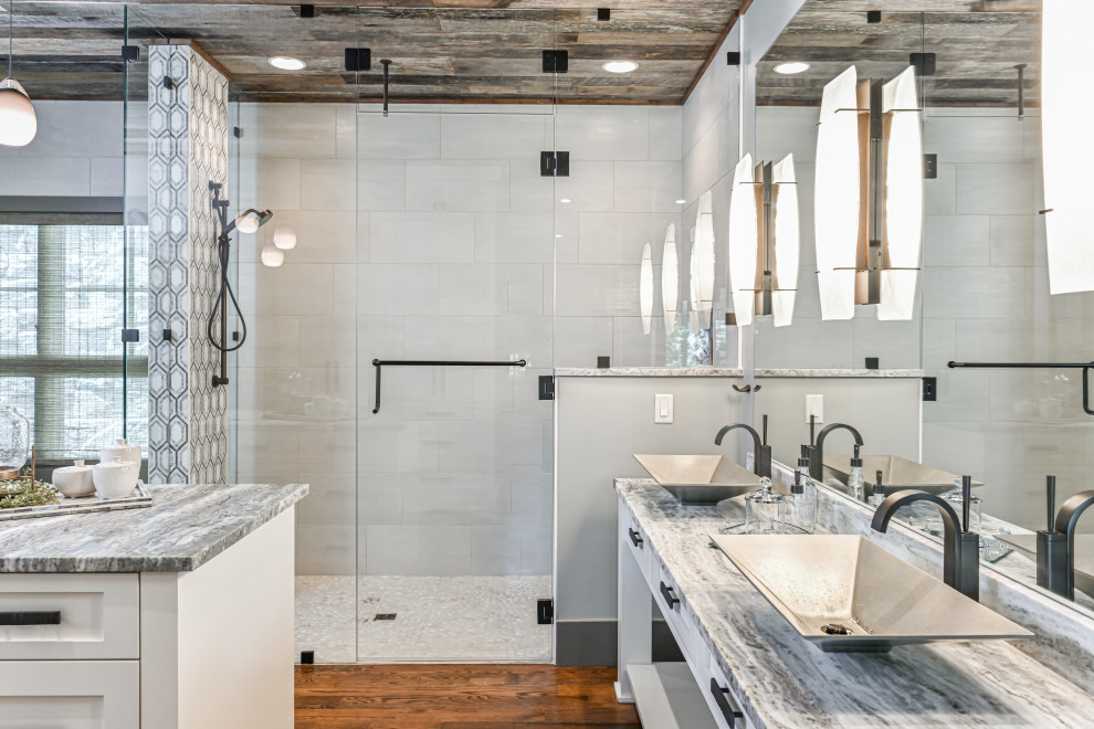 Example of a large minimalist master white tile and porcelain tile dark wood floor and brown floor bathroom design in Other with recessed-panel cabinets, white cabinets, a two-piece toilet, white walls, a vessel sink, marble countertops, a hinged shower door and gray countertops