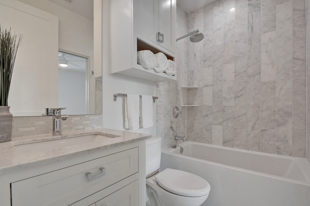 Cette photo montre une salle de bain chic de taille moyenne avec un placard à porte shaker, des portes de placard blanches, une baignoire en alcôve, un combiné douche/baignoire, WC à poser, un mur blanc, un lavabo encastré et un plan de toilette en granite.