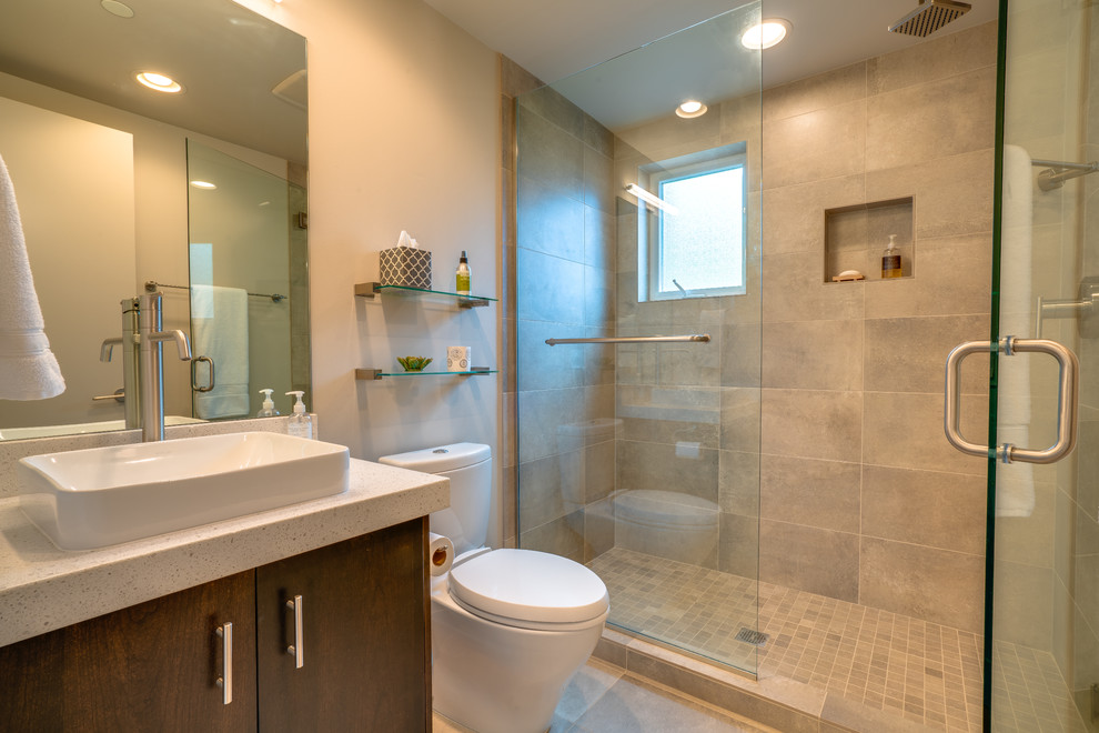 Modernes Badezimmer mit flächenbündigen Schrankfronten, dunklen Holzschränken, Duschnische, grauen Fliesen, beiger Wandfarbe, Aufsatzwaschbecken, grauem Boden, Falttür-Duschabtrennung und weißer Waschtischplatte in Seattle