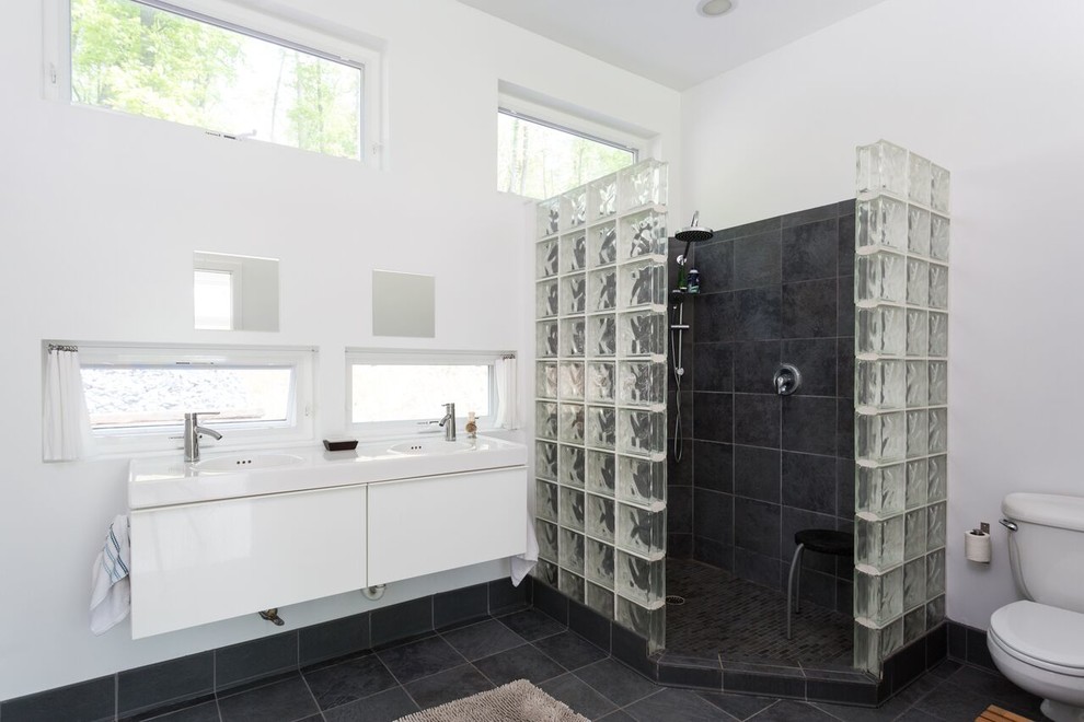 На фото: большая главная ванная комната в стиле модернизм с плоскими фасадами, белыми фасадами, угловым душем, раздельным унитазом, черной плиткой, плиткой из сланца, белыми стенами, полом из сланца, монолитной раковиной, столешницей из кварцита, черным полом и открытым душем