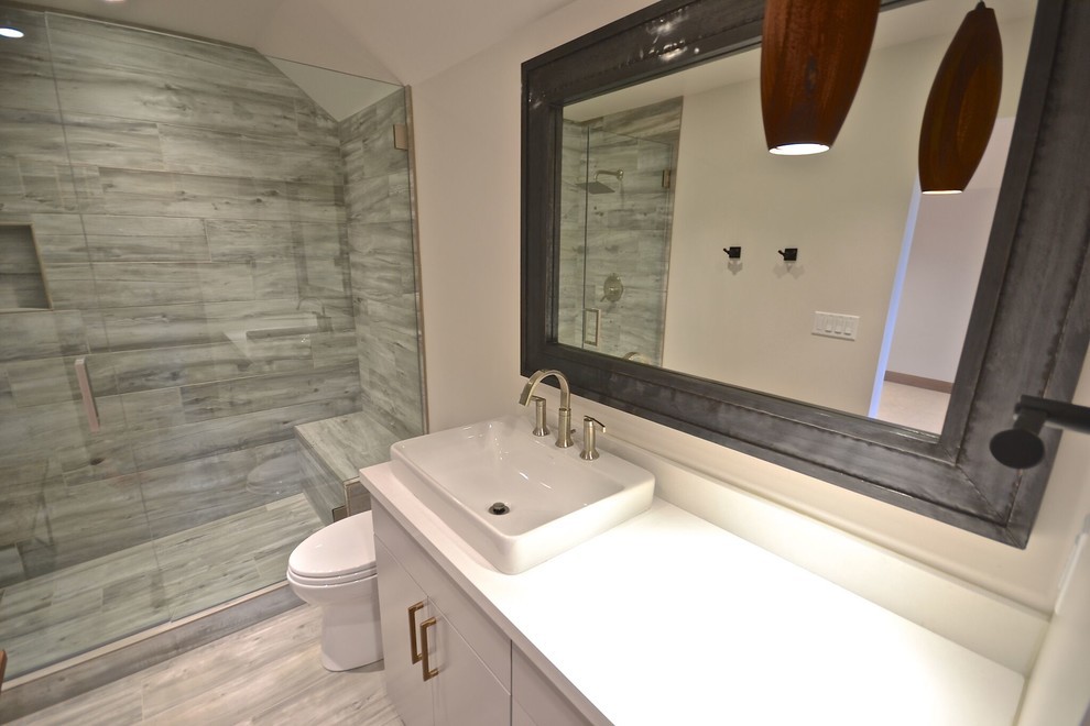 Exemple d'une salle de bain moderne de taille moyenne avec un placard à porte plane, des portes de placard blanches, WC séparés, un carrelage gris, des carreaux de porcelaine, un mur blanc, un sol en carrelage de porcelaine, une vasque, un plan de toilette en surface solide, un sol gris, une cabine de douche à porte battante et un plan de toilette blanc.