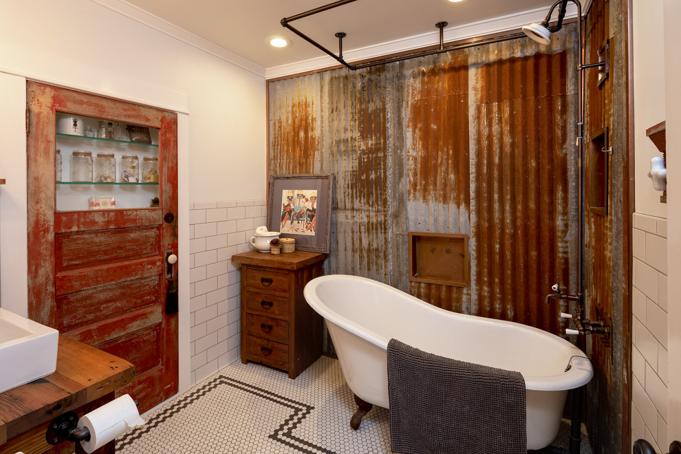 Foto på ett industriellt brun badrum, med ett badkar med tassar, vit kakel, tunnelbanekakel, vita väggar, mosaikgolv, ett fristående handfat, träbänkskiva och vitt golv