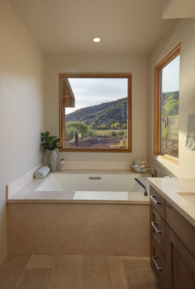 Photo of a large ensuite bathroom in Phoenix with recessed-panel cabinets, brown cabinets, a submerged bath, an alcove shower, a one-piece toilet, beige tiles, porcelain tiles, beige walls, porcelain flooring, a submerged sink, limestone worktops, beige floors, an open shower and beige worktops.