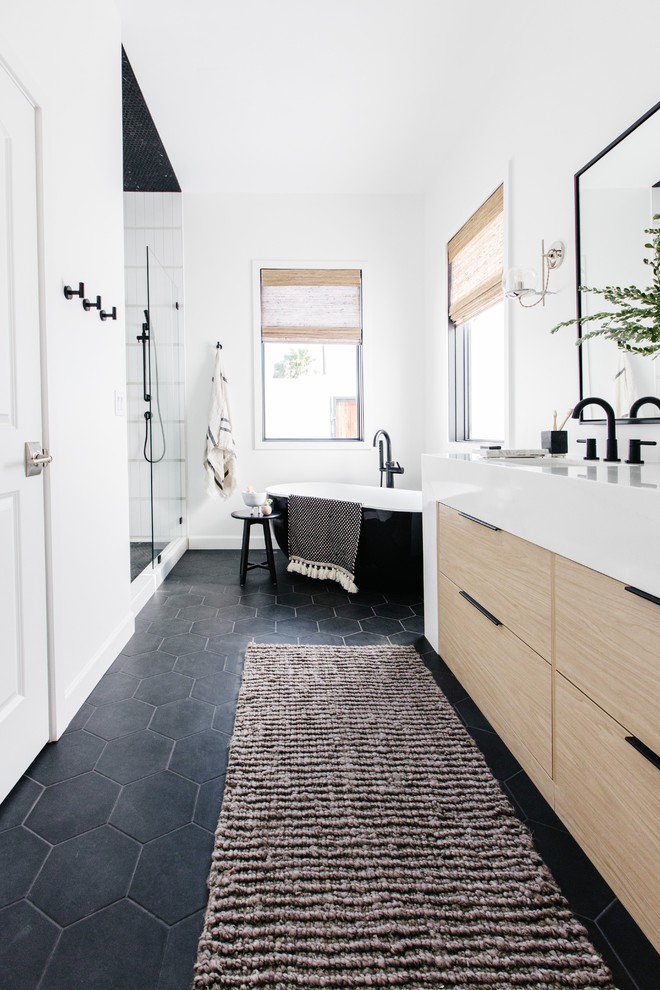 This is an example of a medium sized scandinavian ensuite bathroom in Phoenix with flat-panel cabinets, light wood cabinets, a freestanding bath, an alcove shower, white walls, ceramic flooring, a submerged sink, quartz worktops, black floors, a hinged door and white worktops.