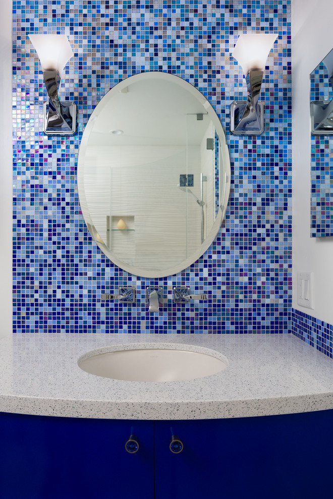 На фото: детская ванная комната среднего размера в морском стиле с плоскими фасадами, синими фасадами, ванной в нише, душем над ванной, унитазом-моноблоком, синей плиткой, стеклянной плиткой, белыми стенами, полом из керамической плитки, врезной раковиной и столешницей из искусственного кварца