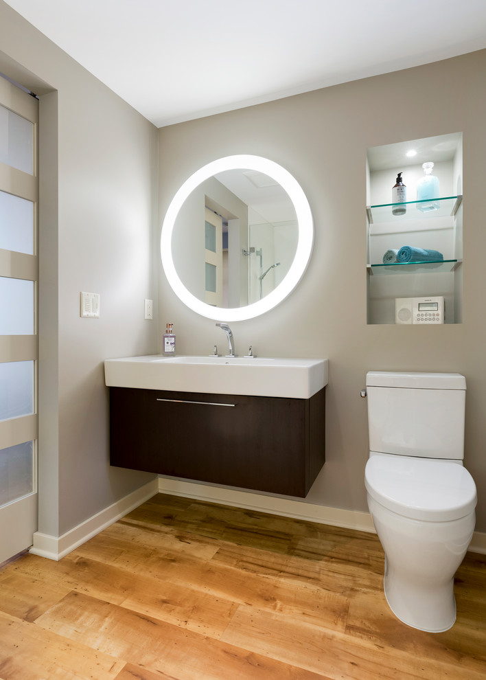 Inredning av ett modernt litet vit vitt badrum med dusch, med släta luckor, bruna skåp, en kantlös dusch, en toalettstol med hel cisternkåpa, grå väggar, vinylgolv, ett väggmonterat handfat, brunt golv och med dusch som är öppen