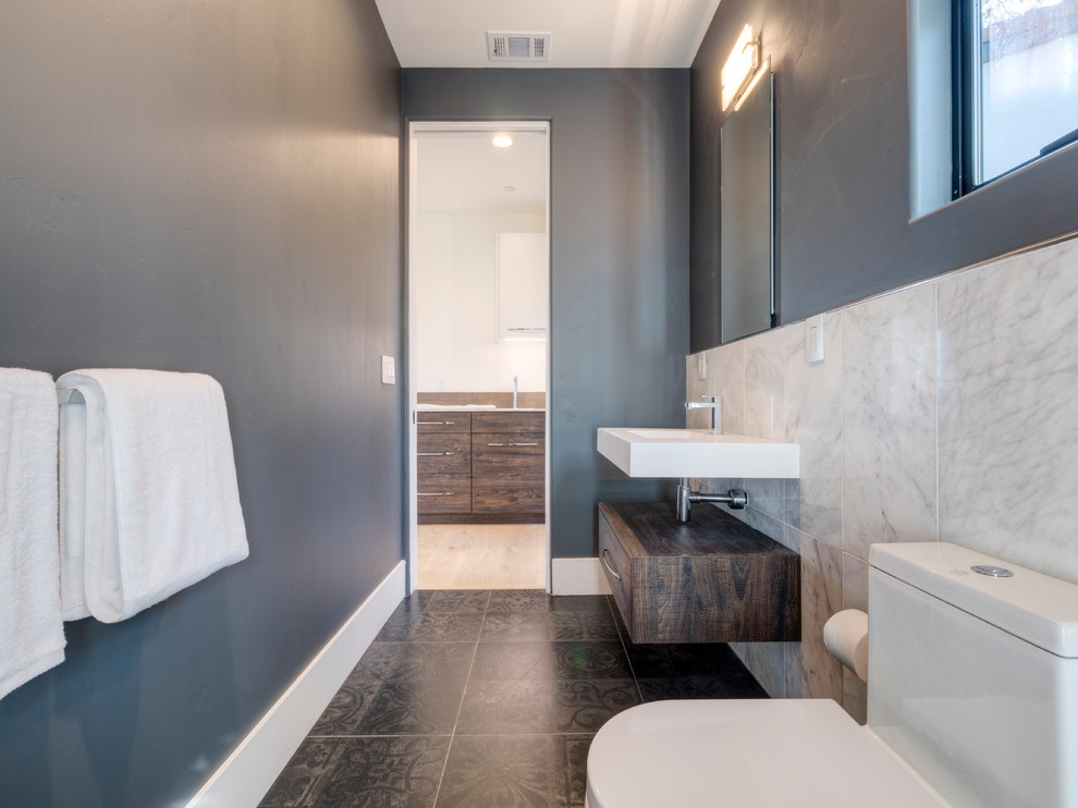 Modern inredning av ett mellanstort badrum med dusch, med en toalettstol med hel cisternkåpa, svart kakel, porslinskakel, vita väggar, klinkergolv i porslin, ett väggmonterat handfat och bänkskiva i akrylsten