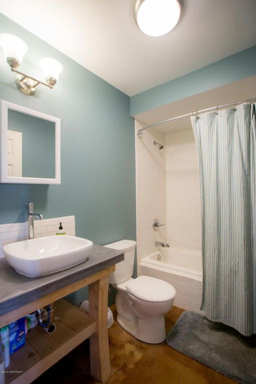 Cette photo montre une grande salle d'eau nature avec des portes de placard marrons, une baignoire en alcôve, un combiné douche/baignoire, WC à poser, un carrelage multicolore, un carrelage en pâte de verre, un mur bleu, sol en béton ciré, une vasque, un plan de toilette en béton, un sol marron, une cabine de douche avec un rideau, un plan de toilette gris, un banc de douche, meuble simple vasque, meuble-lavabo sur pied et un plafond décaissé.