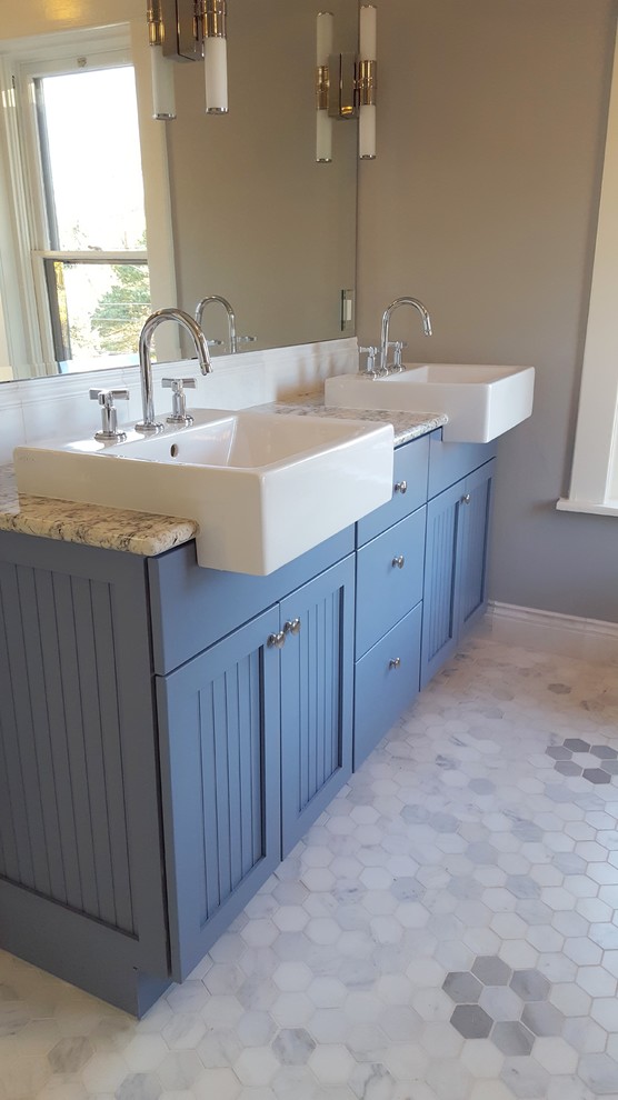 Klassisk inredning av ett en-suite badrum, med luckor med profilerade fronter, blå skåp, ett platsbyggt badkar, en dubbeldusch, en toalettstol med separat cisternkåpa, blå kakel, tunnelbanekakel, grå väggar, marmorgolv och granitbänkskiva