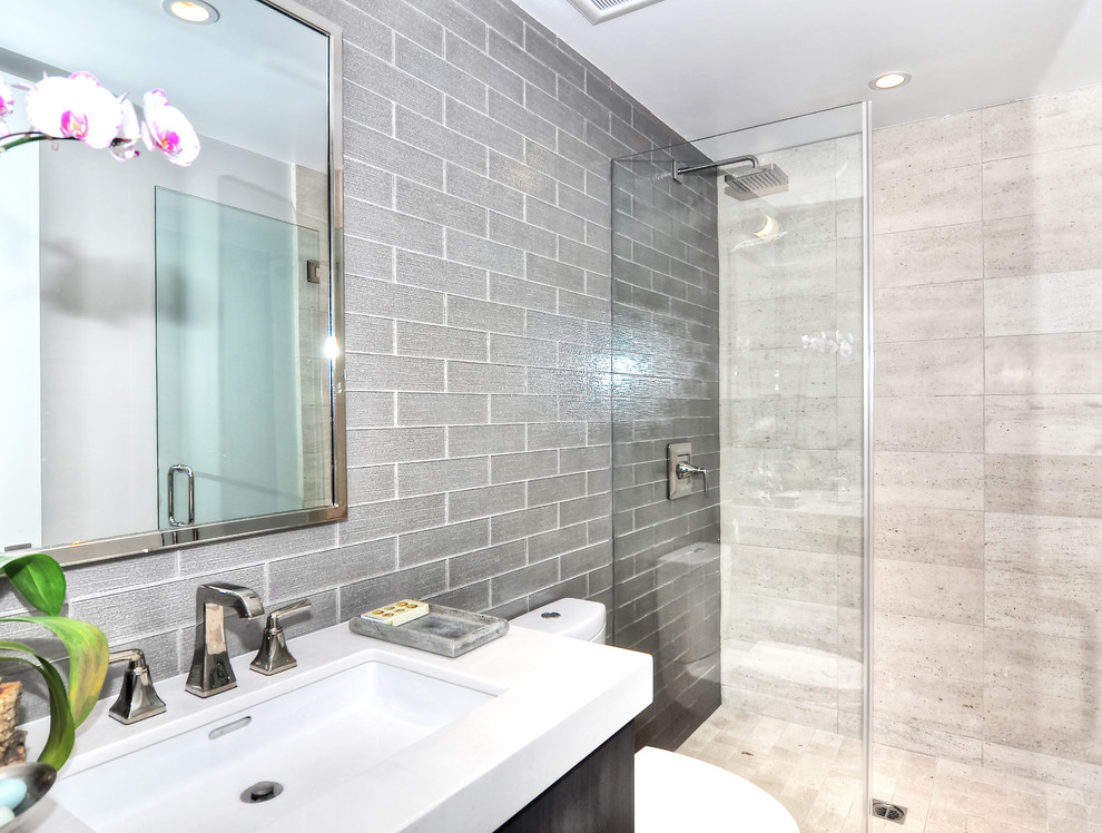 Immagine di una stanza da bagno con doccia minimalista di medie dimensioni con ante lisce, ante in legno bruno, doccia aperta, WC a due pezzi, piastrelle grigie, piastrelle di vetro, pareti bianche, lavabo sottopiano, doccia aperta e top bianco