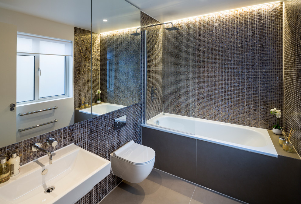 Bild på ett mellanstort funkis badrum, med ett platsbyggt badkar, en dusch/badkar-kombination, en vägghängd toalettstol, brun kakel, mosaik, bruna väggar, klinkergolv i porslin och ett väggmonterat handfat