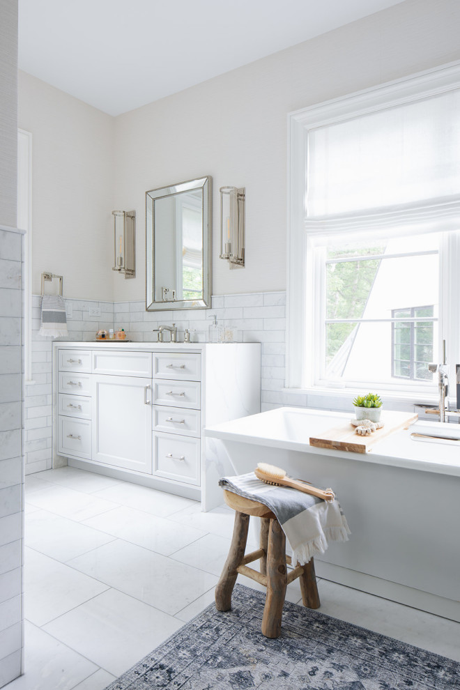 Стильный дизайн: ванная комната в стиле неоклассика (современная классика) с белыми фасадами, отдельно стоящей ванной, белой плиткой, керамической плиткой, бежевыми стенами, полом из керамической плитки, белым полом, белой столешницей и встроенной тумбой - последний тренд