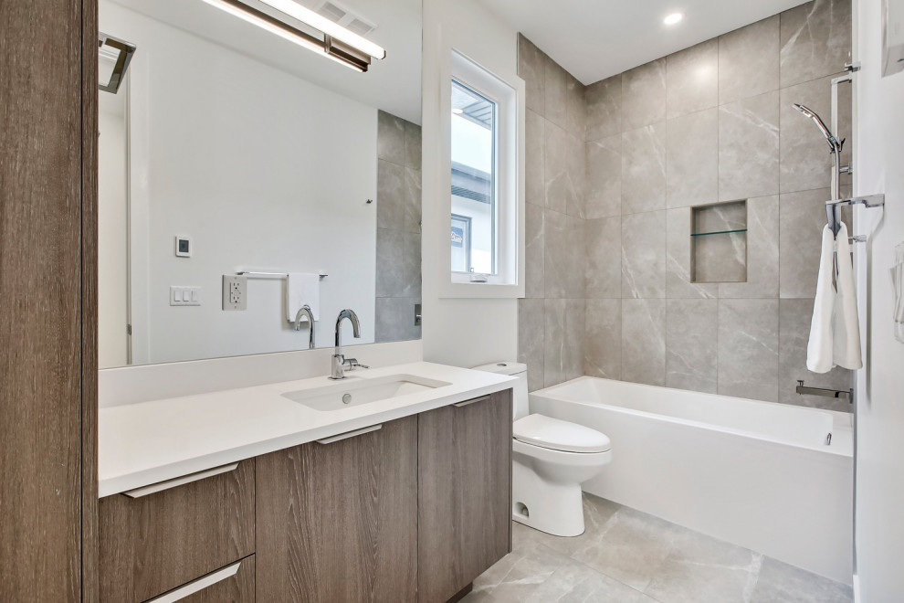 Esempio di una stanza da bagno con doccia design di medie dimensioni con ante lisce, ante grigie, vasca ad alcova, vasca/doccia, orinatoio, piastrelle grigie, pareti bianche, lavabo sottopiano, pavimento grigio e top bianco