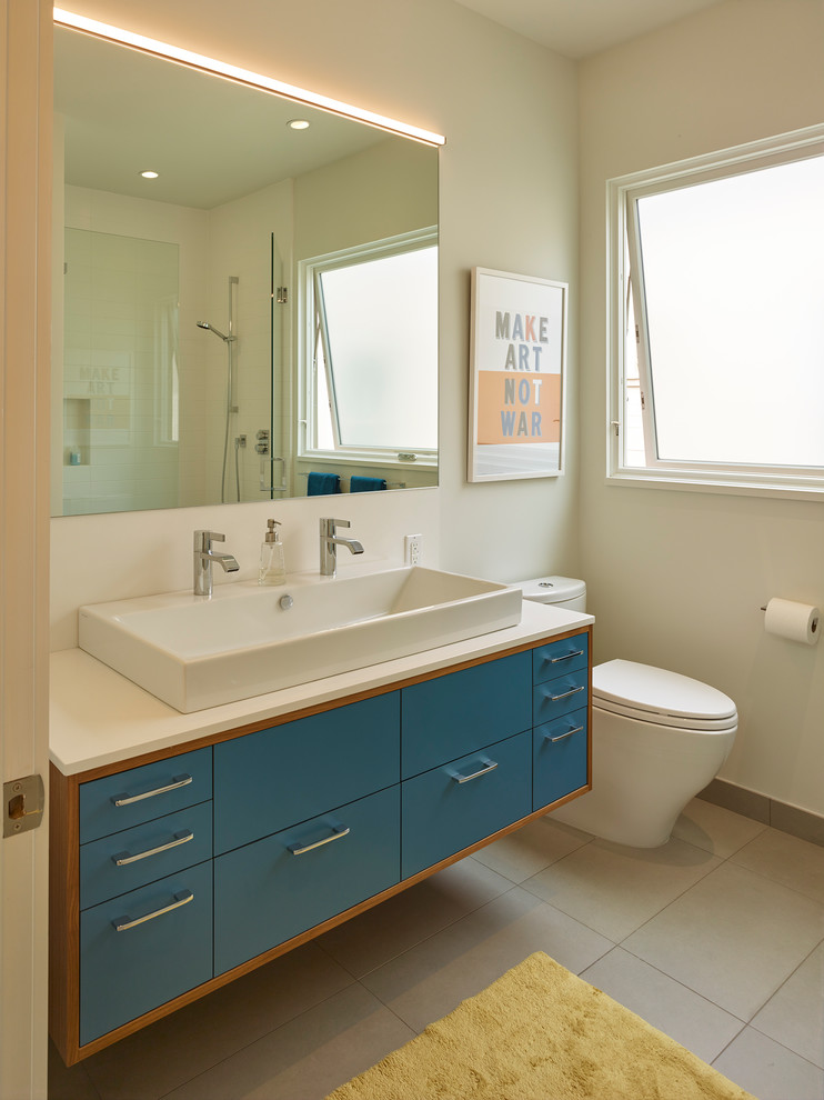 Cette photo montre une salle de bain tendance de taille moyenne avec un placard à porte plane, des portes de placard bleues, WC séparés, un carrelage gris, des carreaux de céramique, un mur beige, un sol en carrelage de céramique, une grande vasque et un plan de toilette en surface solide.