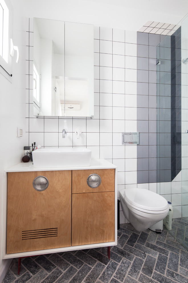 Exemple d'une salle de bain tendance en bois clair avec WC suspendus, un mur blanc, une vasque, un placard à porte plane et un carrelage blanc.
