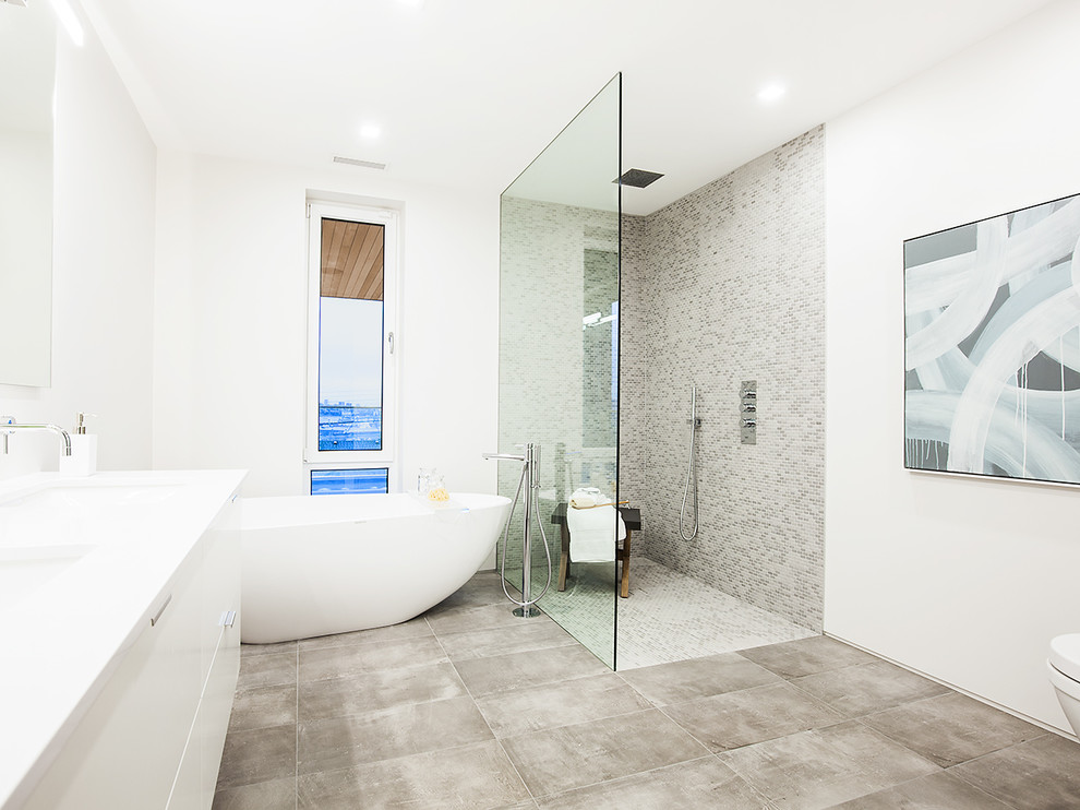 На фото: главная ванная комната в современном стиле с плоскими фасадами, белыми фасадами, отдельно стоящей ванной, душем без бортиков, разноцветной плиткой, плиткой мозаикой, белыми стенами, врезной раковиной, серым полом, открытым душем и белой столешницей с