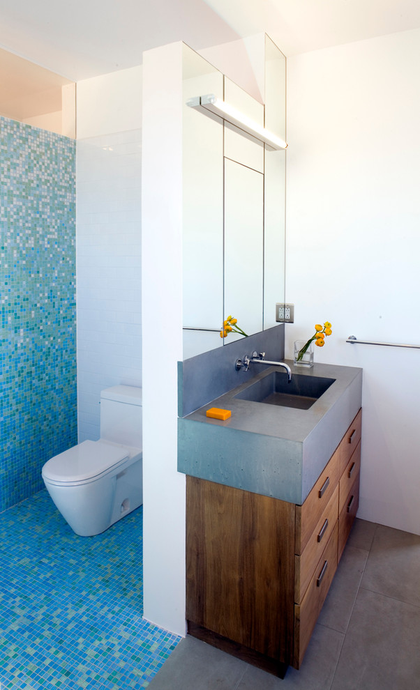 Свежая идея для дизайна: главная ванная комната среднего размера в стиле модернизм с плоскими фасадами, фасадами цвета дерева среднего тона, накладной ванной, душем над ванной, синей плиткой, стеклянной плиткой, полом из керамогранита, монолитной раковиной, столешницей из бетона и унитазом-моноблоком - отличное фото интерьера