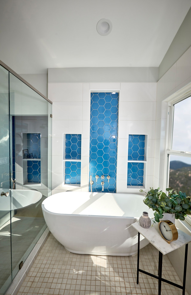 На фото: большая главная ванная комната в стиле модернизм с плоскими фасадами, светлыми деревянными фасадами, отдельно стоящей ванной, душевой комнатой, унитазом-моноблоком, синей плиткой, стеклянной плиткой, белыми стенами, полом из керамогранита, врезной раковиной, столешницей из искусственного кварца, белым полом, душем с распашными дверями и белой столешницей