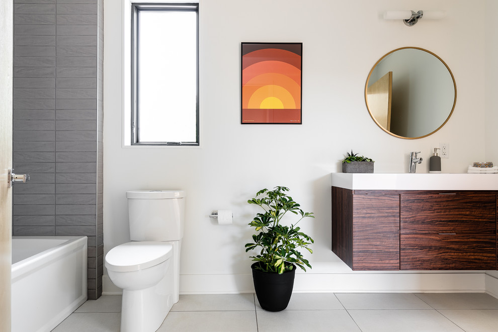 Foto på ett funkis badrum, med grå kakel, grå väggar, släta luckor, skåp i mörkt trä, ett badkar i en alkov, en dusch/badkar-kombination, en toalettstol med separat cisternkåpa och med dusch som är öppen
