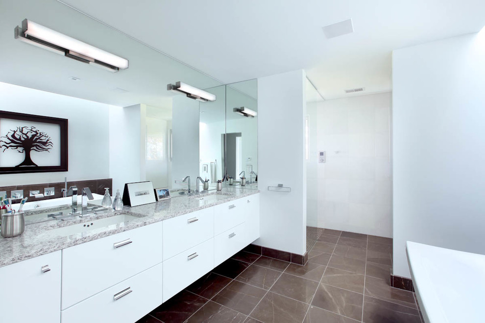 Example of a trendy master brown tile bathroom design in Grand Rapids with an undermount sink, flat-panel cabinets, white cabinets, solid surface countertops, a two-piece toilet and white walls