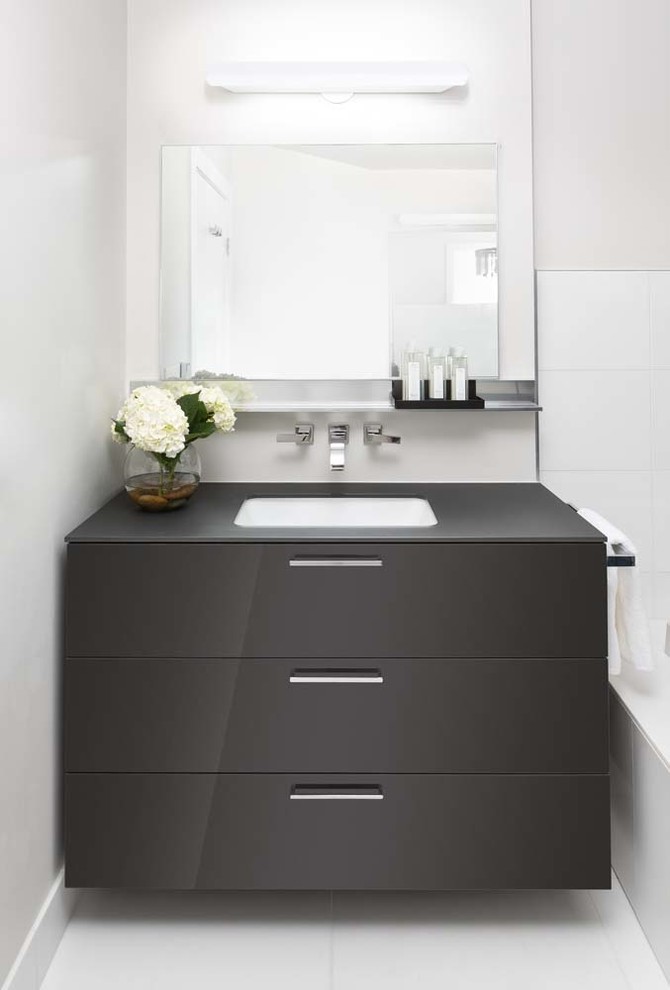 Cette image montre une salle de bain principale design de taille moyenne avec un placard en trompe-l'oeil, des portes de placard grises, un plan de toilette en verre et un sol en bois brun.
