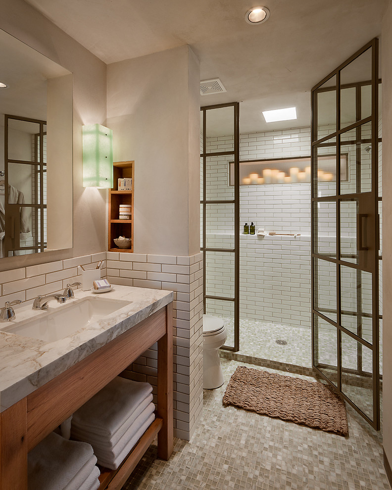 Example of a mid-sized trendy 3/4 white tile ceramic tile alcove shower design in Phoenix with a drop-in sink, open cabinets, light wood cabinets, marble countertops and beige walls