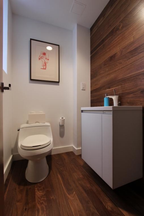 Cette image montre un petit WC et toilettes minimaliste avec un placard à porte plane, des portes de placard blanches et un sol en bois brun.