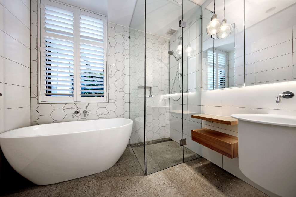 Bild på ett funkis badrum, med ett fristående badkar, en hörndusch, vit kakel, ett väggmonterat handfat, grått golv och dusch med gångjärnsdörr