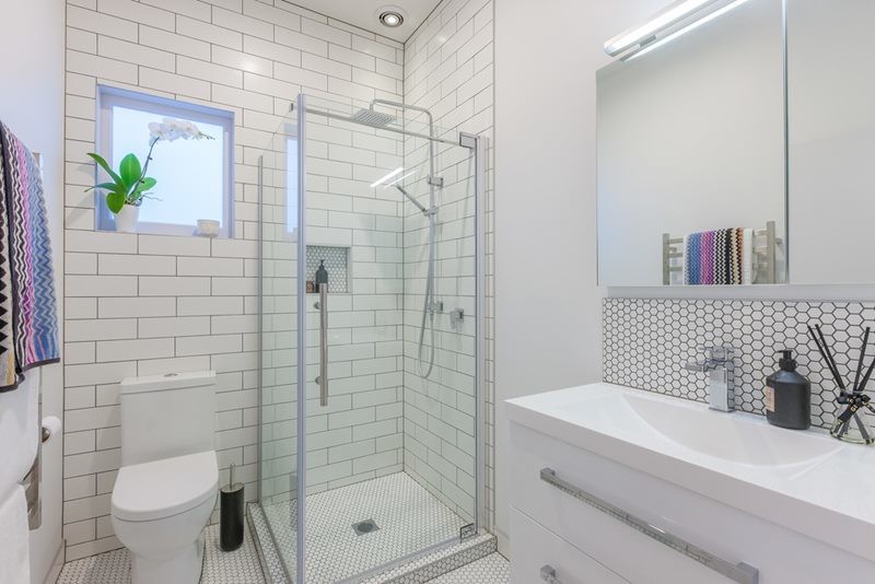 Small contemporary ensuite bathroom in Auckland with white cabinets, a corner shower, a one-piece toilet, white tiles, ceramic tiles, white walls, ceramic flooring, a wall-mounted sink, white floors and a hinged door.