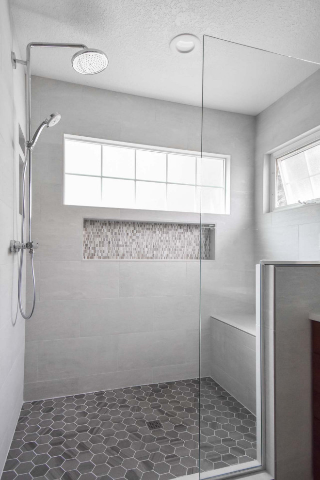 На фото: большая главная ванная комната в стиле модернизм с фасадами с утопленной филенкой, фасадами цвета дерева среднего тона, душем в нише, раздельным унитазом, серой плиткой, керамической плиткой, серыми стенами, полом из керамической плитки, врезной раковиной, столешницей из искусственного кварца, серым полом, душем с распашными дверями, белой столешницей, сиденьем для душа, тумбой под одну раковину и встроенной тумбой с