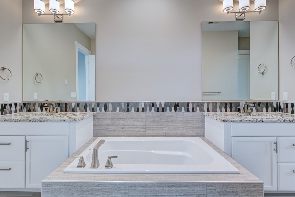 Example of a mid-sized transitional master gray tile and mosaic tile porcelain tile and gray floor drop-in bathtub design in Seattle with recessed-panel cabinets, white cabinets, a two-piece toilet, gray walls, an undermount sink, granite countertops, a hinged shower door and white countertops