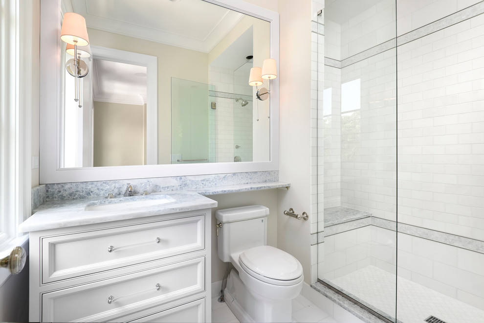 Cette image montre une grande douche en alcôve traditionnelle avec un lavabo encastré, un placard à porte affleurante, des portes de placard grises, un plan de toilette en marbre, WC à poser, un carrelage blanc, un carrelage de pierre, un sol en marbre et un mur blanc.