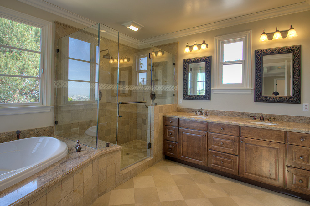 Immagine di una stanza da bagno chic con lavabo sottopiano, ante con bugna sagomata, vasca da incasso, doccia ad angolo, piastrelle beige e ante in legno bruno
