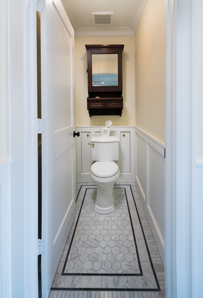 Exemple d'un WC et toilettes chic de taille moyenne avec un placard à porte shaker, des portes de placard blanches, un carrelage gris, un mur jaune et un sol blanc.