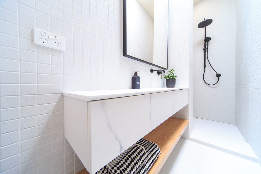 Exemple d'une salle de bain tendance de taille moyenne avec un placard à porte plane, des portes de placard blanches, une douche ouverte, un carrelage blanc, un mur blanc, un lavabo intégré, un plan de toilette en marbre, un sol blanc et aucune cabine.