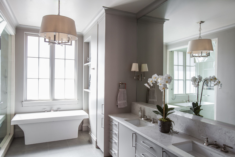Ejemplo de cuarto de baño clásico renovado con armarios con paneles lisos, puertas de armario grises, bañera exenta, paredes grises y lavabo bajoencimera